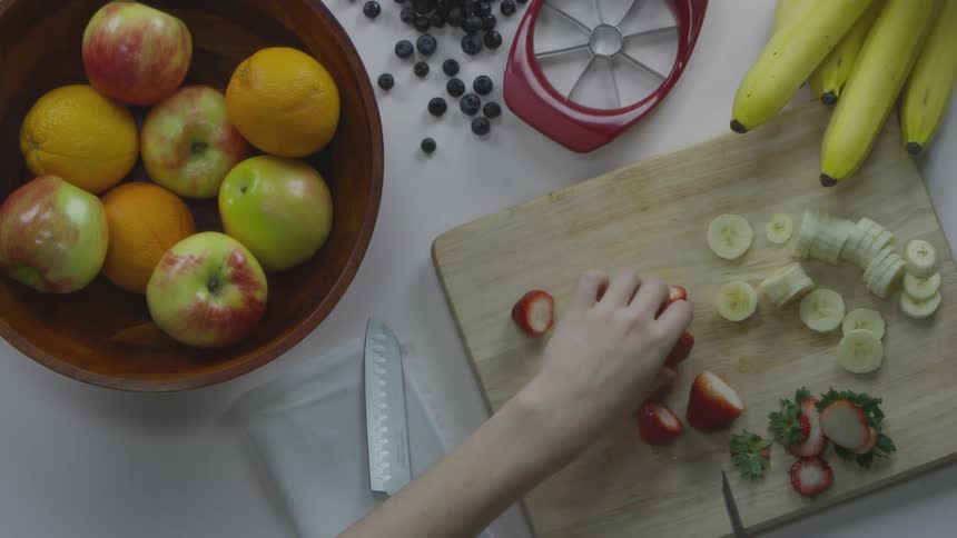 A person is cutting fruits with a knife on a cutting board