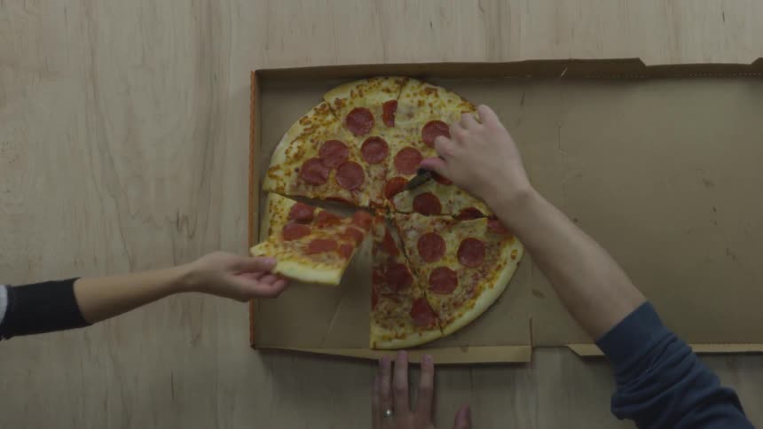 Woman takes one piece of pizza from the pizza box while man is cutting the pizza