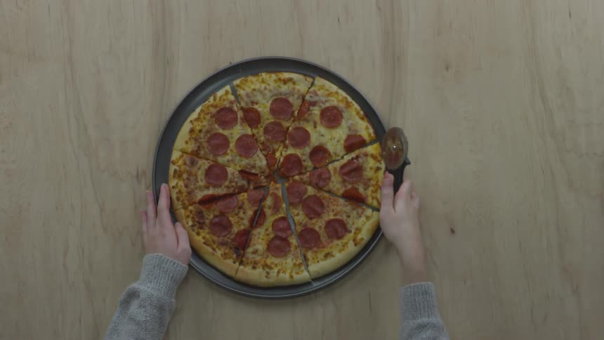 A person finishes slicing a pizza and arranges the slices on the round tray