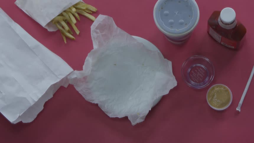 Person unwraps a burger on a plate and takes a bite