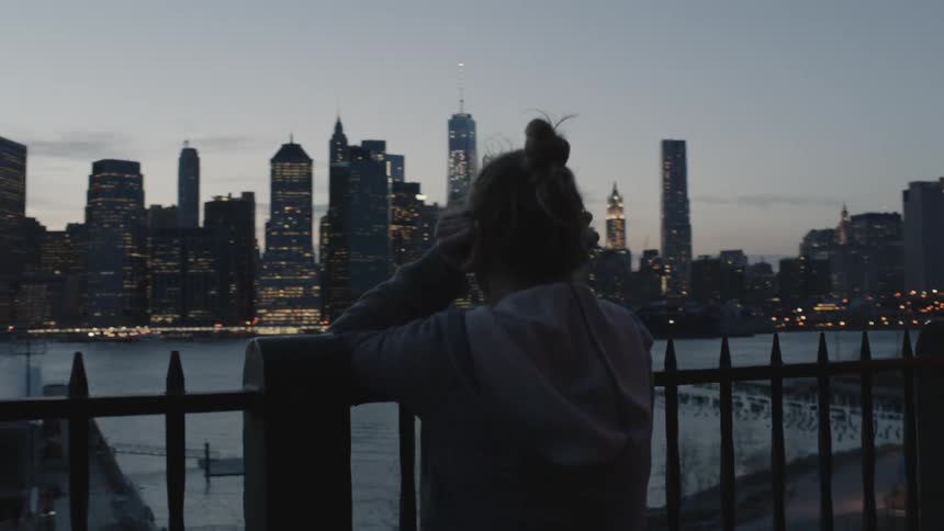 A woman stands by a railing overseeing a city at sunset
