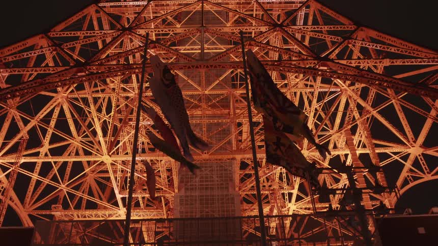 Flags and windsocks fly in front of illuminated tokyo tower at night