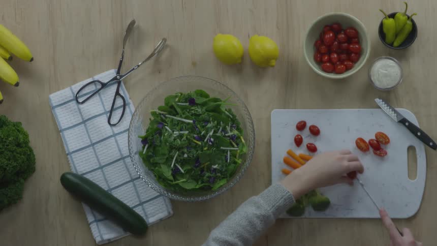 A person cutting tomatoes on a cutting board surrounded by other vegetables