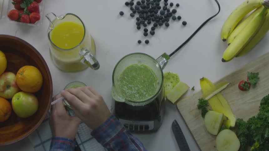 Person puts down green smooth glass next to blender with smoothie in it