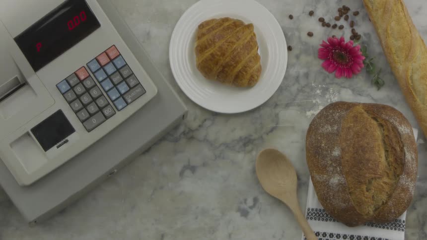 A person sitting a drink and a croissant on a table near bread