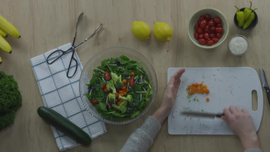 Woman places chopped vegetables in salad