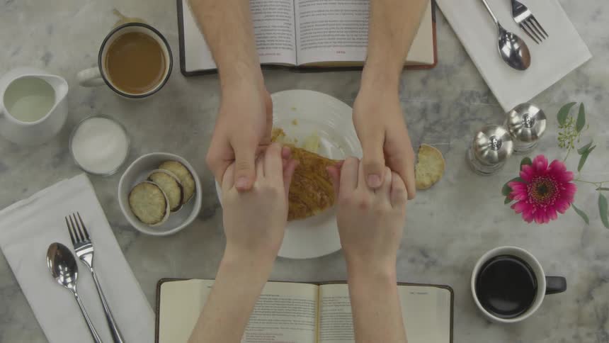 Two people are holding hands across a table of drinks and food