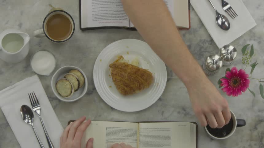 Two people eat breakfast and drink coffee at a table while reading books