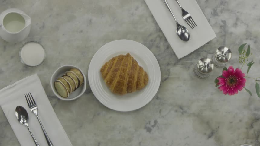 A pastry and cup of coffee are placed on a set table with silverware and napkins