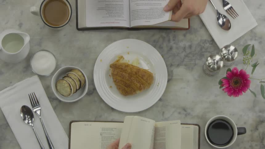 Man and woman are reading book and turning over pages at breakfast table