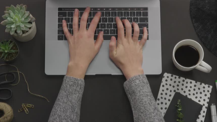 A person in a grey jumper types on a laptop on a dark table