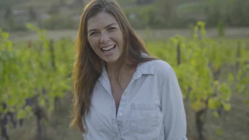 Woman with long hair laughing while standing in a vineyard