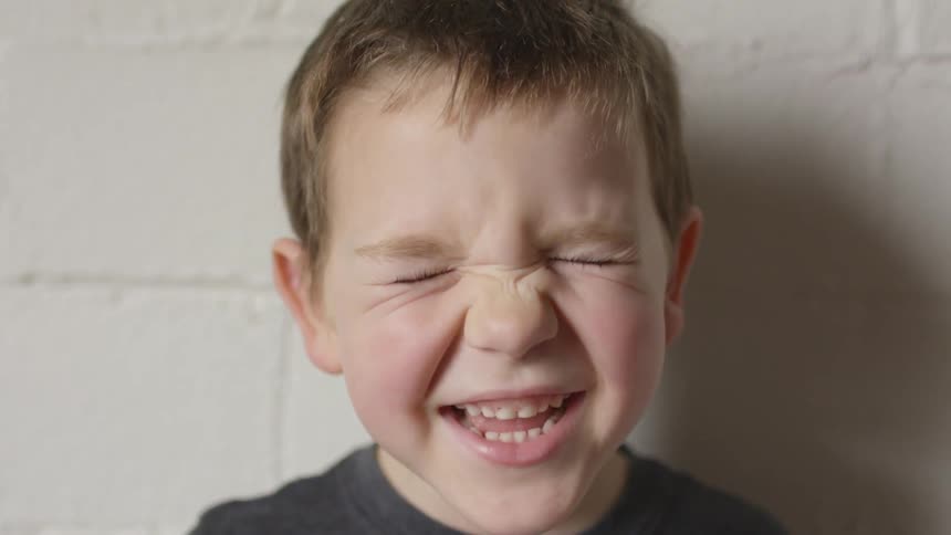 A young boy tightly closes his eyes and smiles while speaking