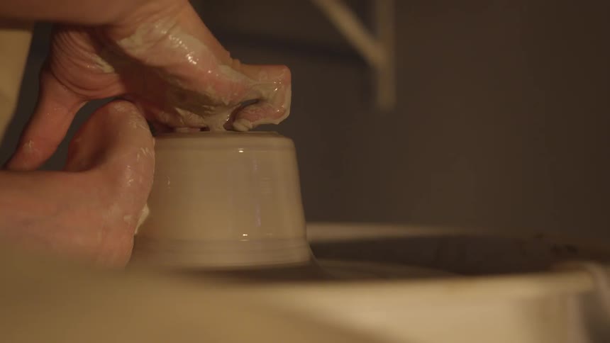 A potter uses his fingers to shape an opening into clay on a potter's wheel