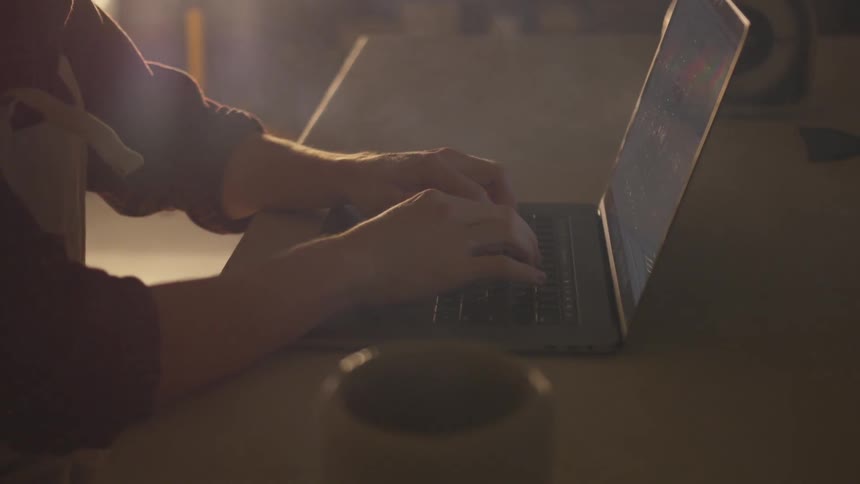 Person types on laptop in dim room