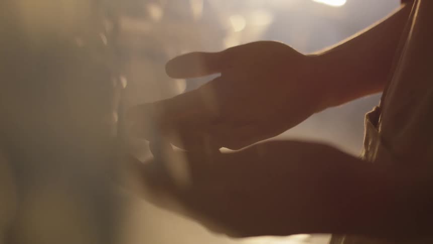 A man wearing an apron stands with his hand palm up in the sunlight of his studio