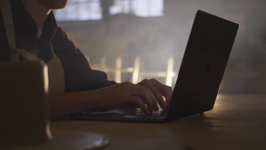 A person types on a laptop in a dimly lit room