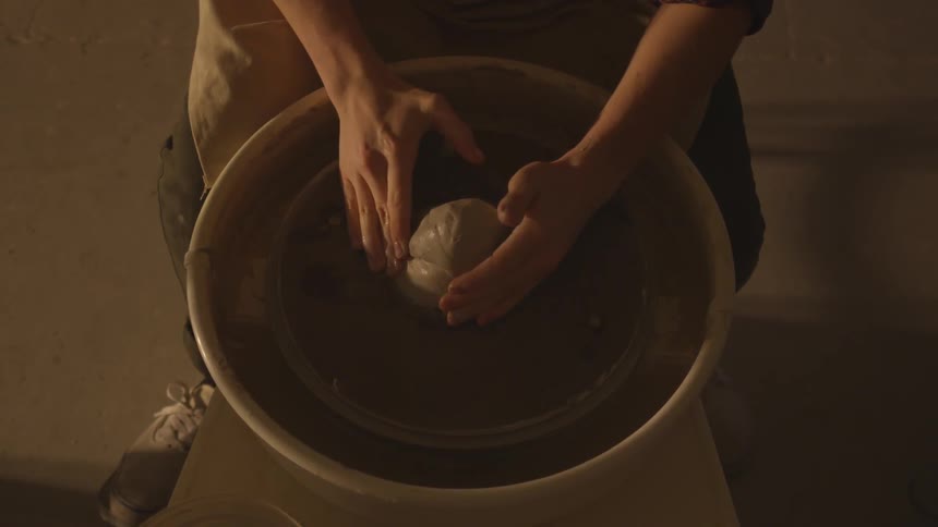 A man with rolled up sleeves carefully molds a wet mass of clay as it sits upon a pottery wheel