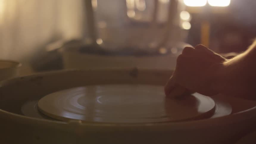 A person rubs clay on a pottery wheel as it spins