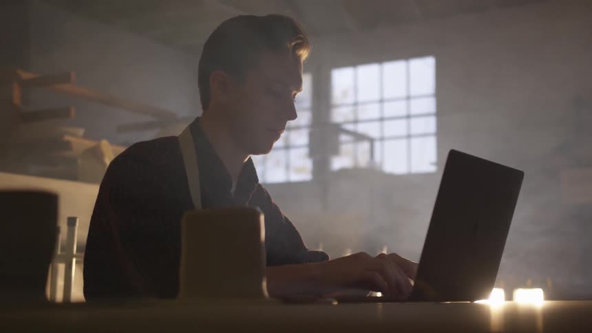 Man sits in a smoky room typing on a laptop