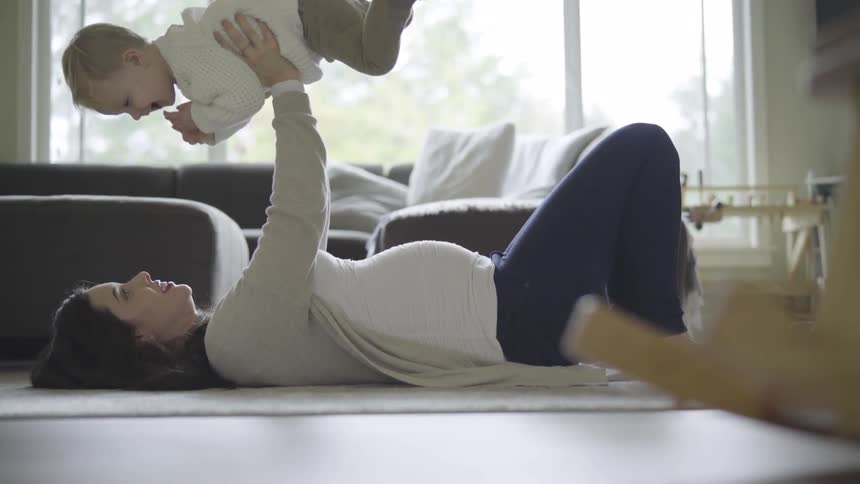Pregnant woman lies down and lifts up baby in the living room