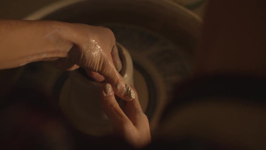 Potter shapes the clay product with pottery tools on the potter's wheel at dusk
