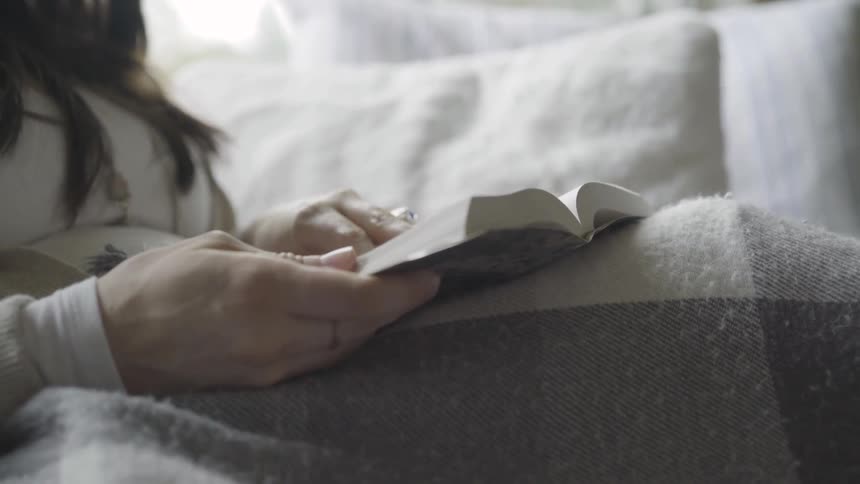 A woman sitting on a sofa turns a page in a small book