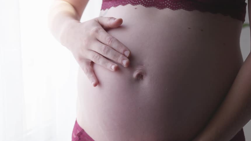 Pregnant women holding her belly while running hand over it in her underwear