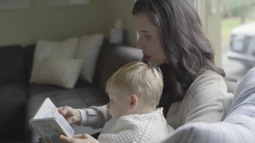 A woman sitting on a couch reading to a toddler