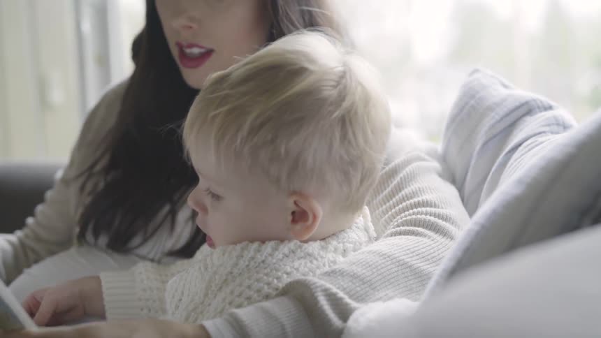 Pregnant woman sits down and reads book for toddler by day