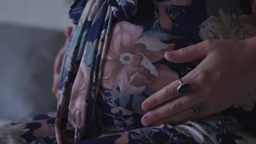 A pregnant woman in a flowered dress caresses and rubs her belly