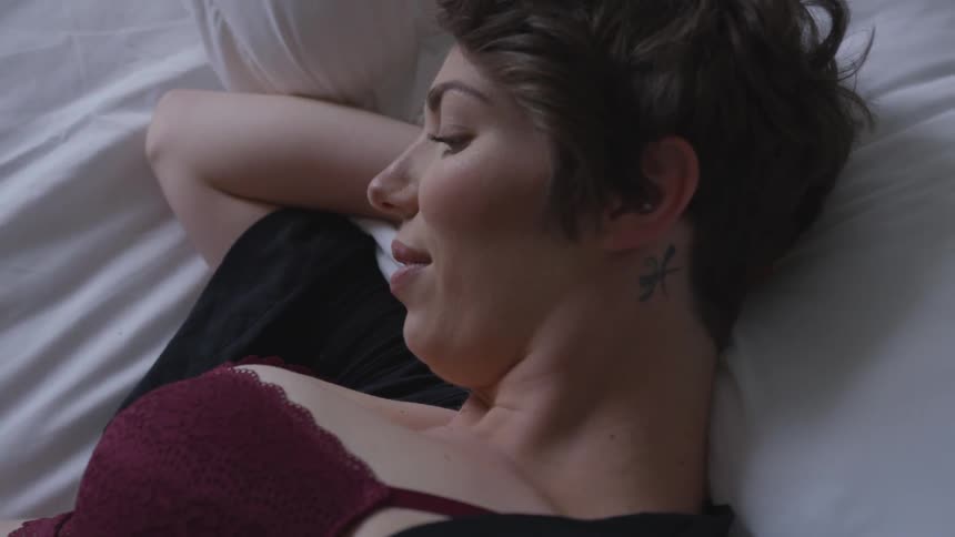 Woman with short dark hair relaxing on bed wearing a red bra