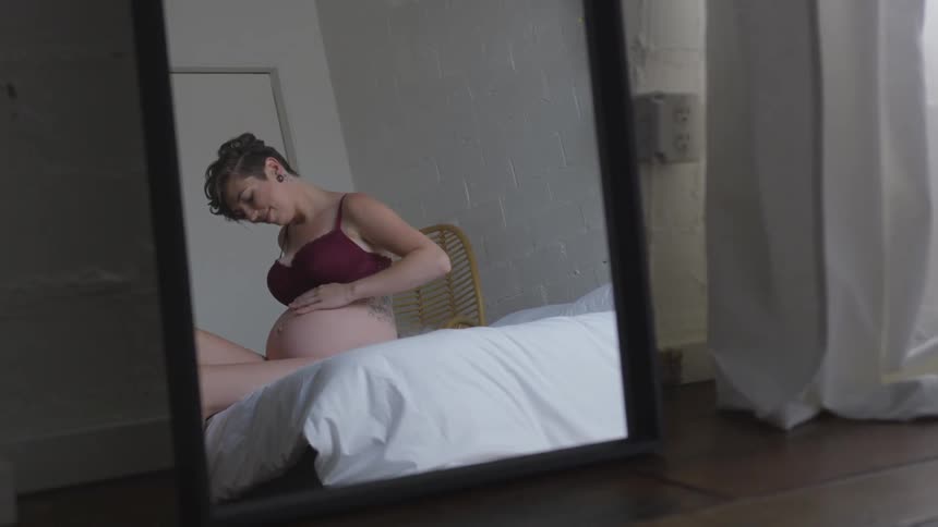 A pregnant woman is sitting on a bed rubbing her stomach
