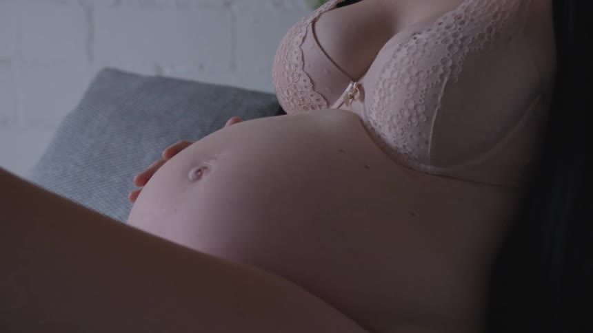 Pregnant woman wearing bro touches her belly during the daytime