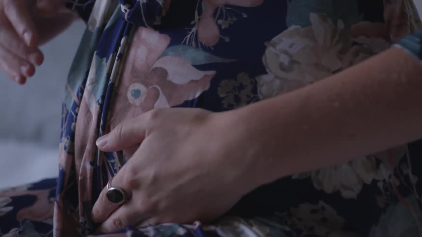 A woman in a floral dress rubs her pregnant stomach