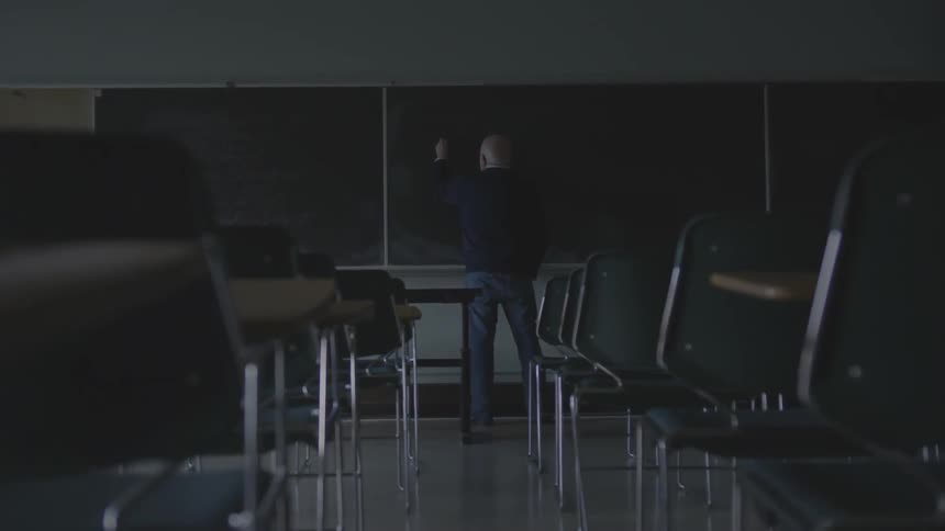 A man writing on a chalkboard in a classroom
