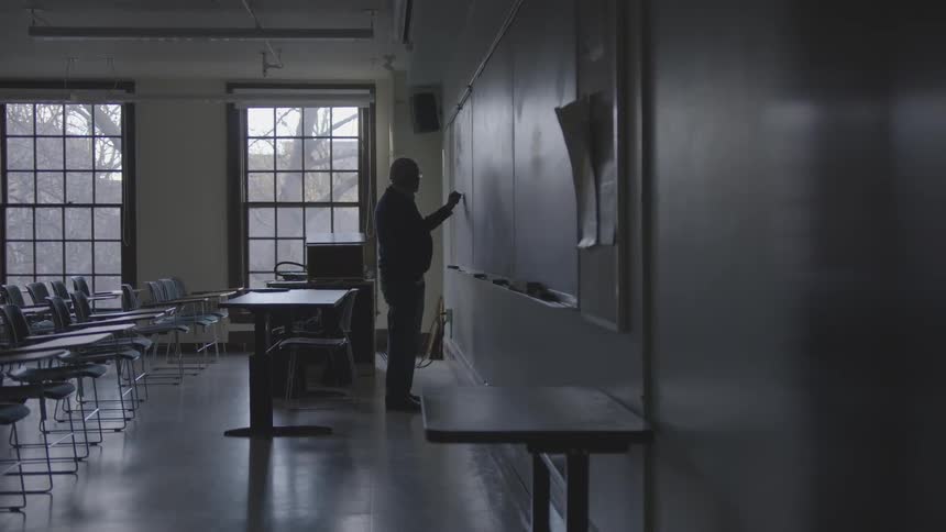 A man in a school classroom writing on a chalkboard