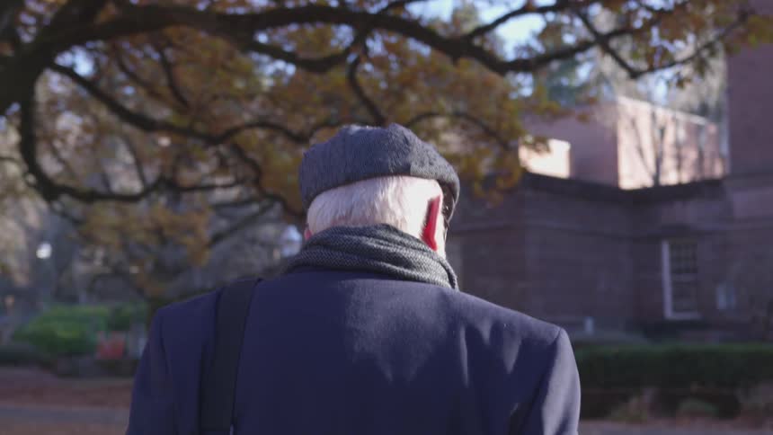 Older man in cap walks along sidewalk