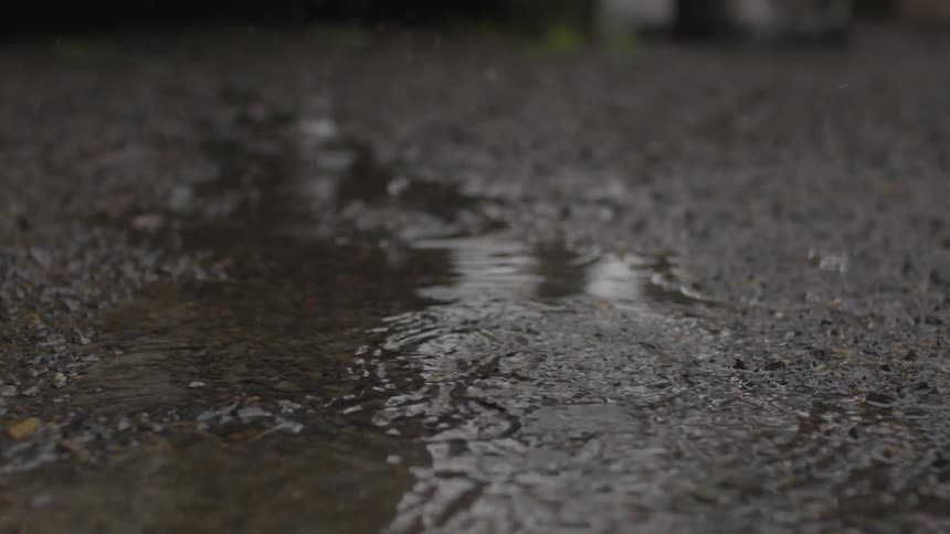 Water drops splash into a puddle on a driveway