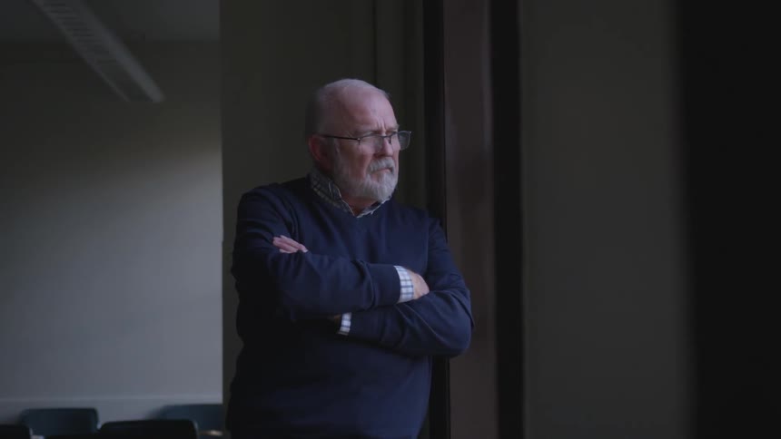A man is crossing his arms and looking out a window