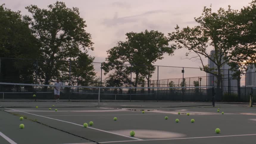 A man is hitting tennis balls on a court on a cloudy day