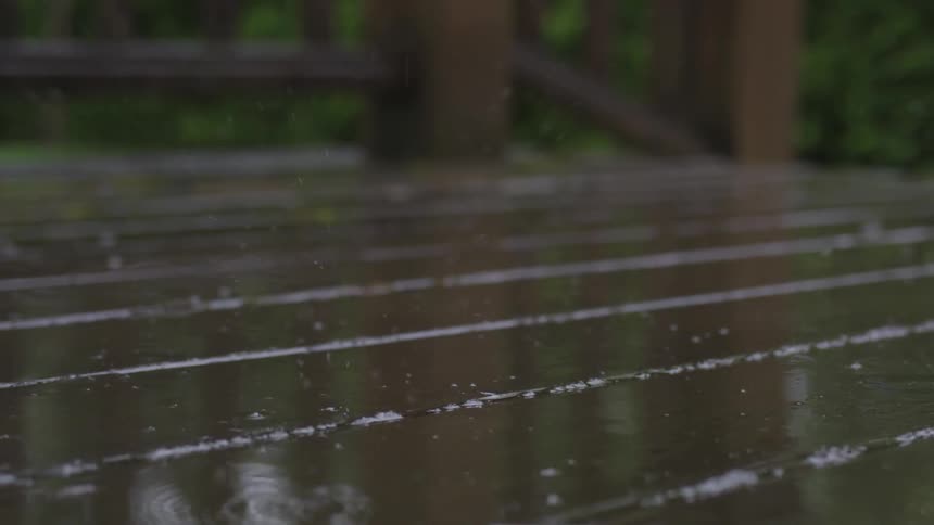 Rain drops fall and splatter onto a wooden deck