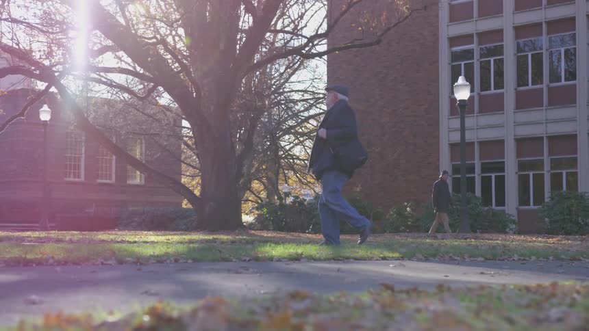 An elderly man walks on a college campus on an autumn day