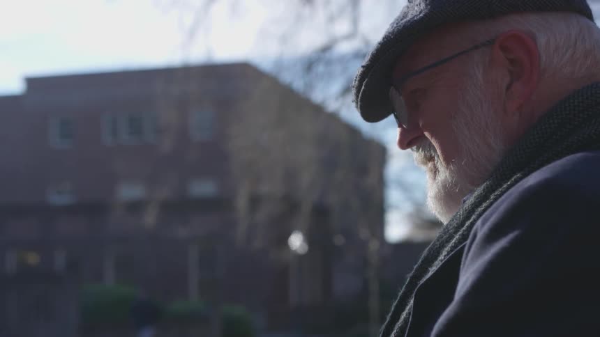 Elderly man in glasses standing near a building