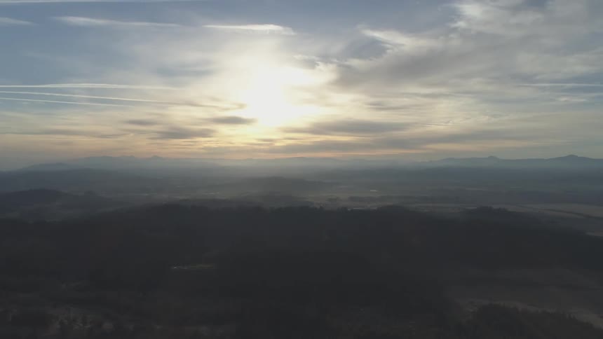 A rural and hilly landscape is viewed from the air at low sun