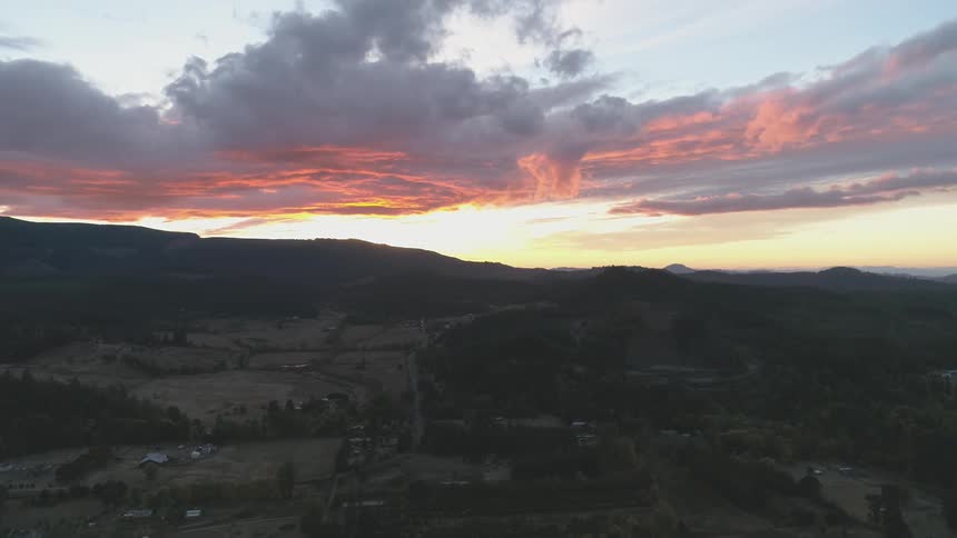 An aerial view of a rural area with hills in the background and pink clouds in the sky