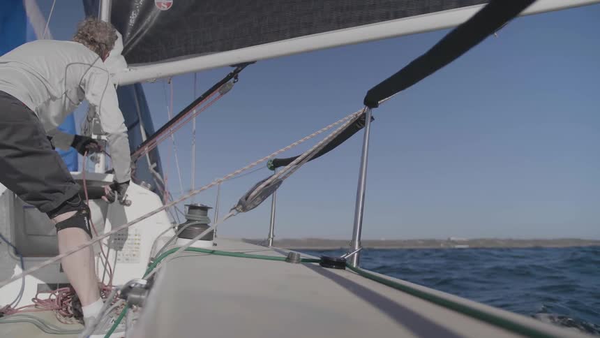 A man in shorts sails a boat towards land in smooth waters under a clear blue sky