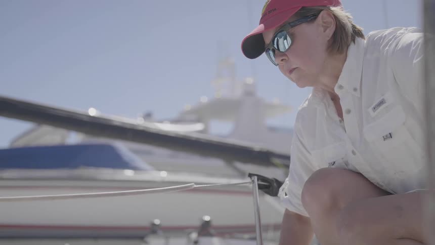 A woman on a boat pulls red rope up and through her hands on a sunny and windy day