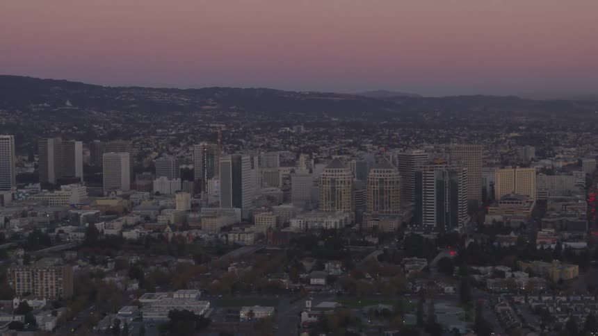 A city with both tall and short buildings with trees hills and roads during sunset