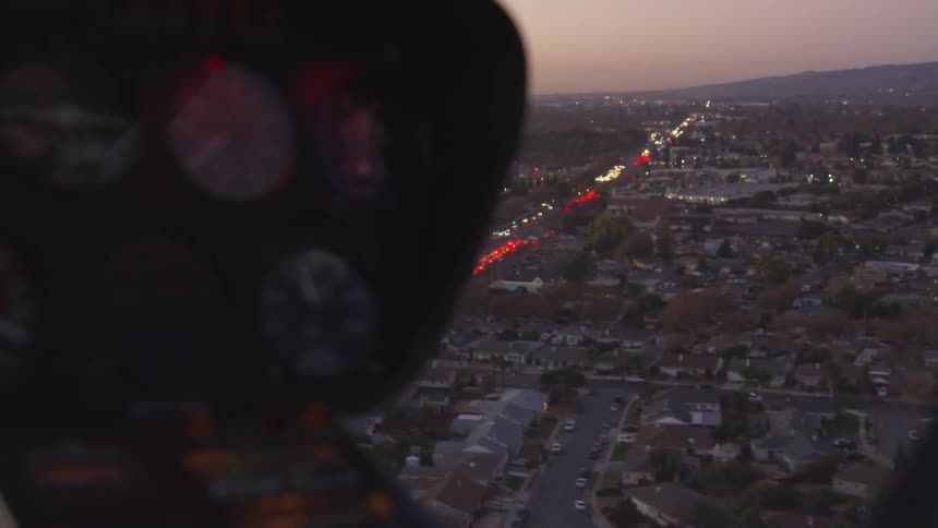 Flying over stream of vehicles with their lights on at sunset during rush hour
